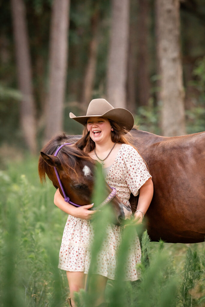 A little girl laughing standing next to her horse