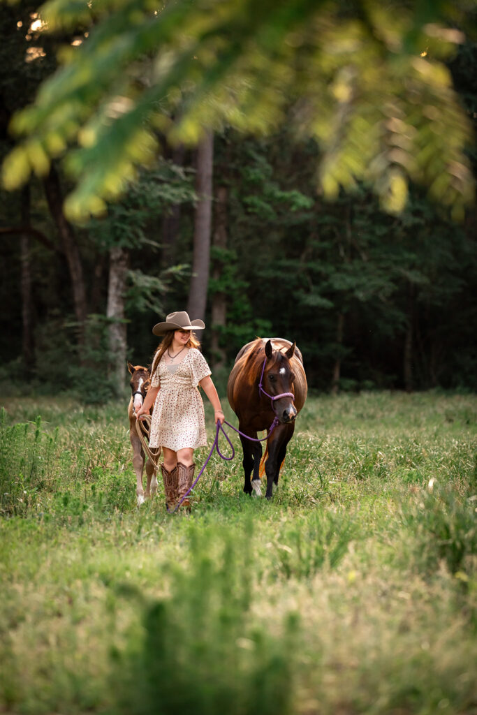 A little girl walking her two horse's through the woods